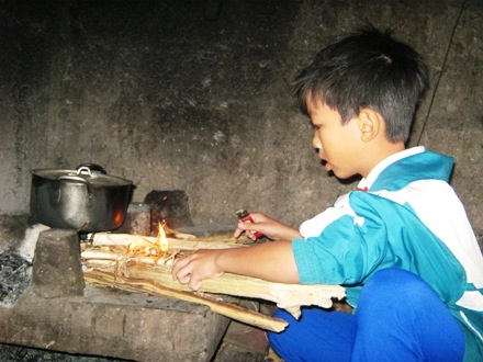 Em Hùng lúi húi nhen lửa nấu lại nồi cháo cho bà nội