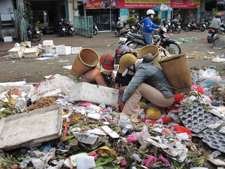 Những người phụ nữ nói tiếng J'rai đang bới đống rác để nhặt trái cây hỏng về ăn