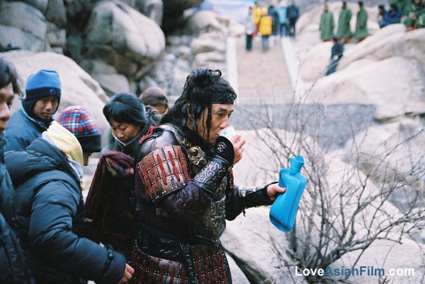 Thành Long uống nước nóng để sưởi ấm cho cơ thể trong giờ nghỉ giải lao