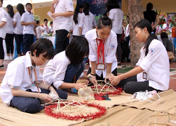 
Ở một góc sân “lặng lẽ” hơn, những cô gái khéo léo chăm chú học cách đan lạt, dán giấy trang kim cho chiếc đèn ông sao truyền thống

