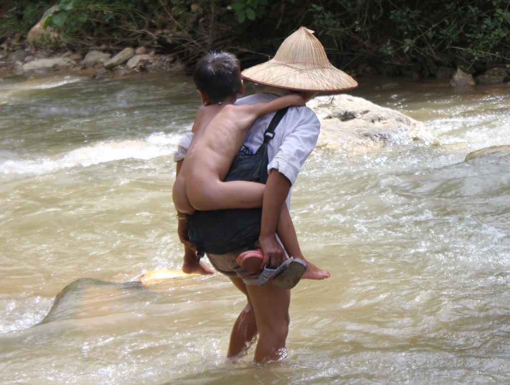 Vượt núi, vượt hồ tìm con chữ của học sinh bản Xốp Cháo, Cà Moong - 4 Xeo Thị Hoa cõng con qua suối. Từ nhà Hoa đến lớp của con phải đi hơn 5km đường rừng, mấy cây số lòng hồ và lội qua 2 quãng suối.