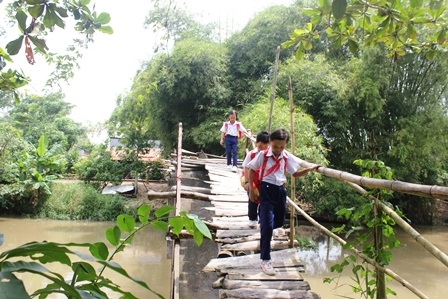 Học sinh tiểu học đi bộ, dắt xe đạp qua cây cầu cũ nát rất nguy hiểm.