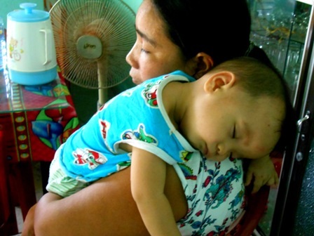 Bé Định Tạo ngủ trên vai mẹ sau một hồi mệt mỏi vì bệnh hành hạ, mô hôi em cứ chảy suốt dù nắng hay mưa, đã nhiều tháng tuổi nhưng Tạo vẫn chưa chập chững được như trẻ khác vì sức khỏe quá yếu