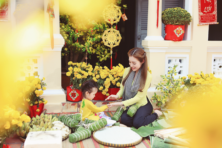 Riêng bé Cadie Mộc Trà, với trang phục tông xuyệt tông cùng mẹ, khoe vẻ đáng yêu, nụ cười tươi tắn như thiên thần. Cô bé còn cùng mẹ thực hiện những động tác gói bánh Tét.