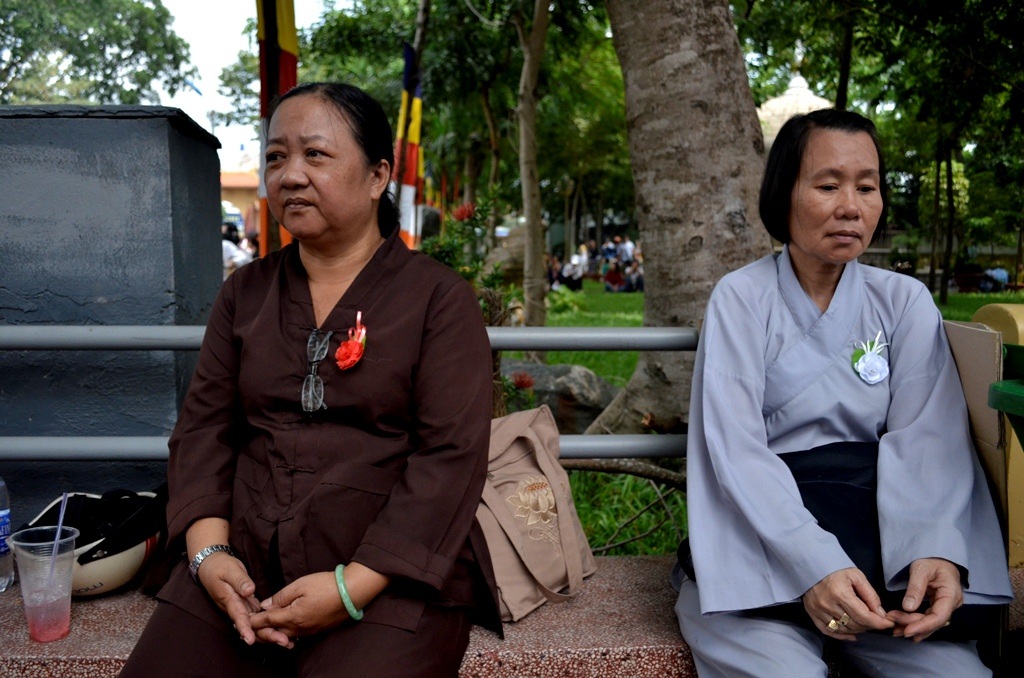 Hai người phụ nữ ngoài năm mươi này không đi chung, họ không hề quen nhau, chỉ tình cờ ngồi cạnh nhau. Tiếp xúc với chúng tôi, người phụ nữ bên trái “định” là sẽ vui, nhưng khi thấy cành hoa trắng của người đồng đạo, cô im lặng. Không có ngôn ngữ nào biểu đạt sự đồng cảm trong tình huống này. Và cũng càng không thể hạnh phúc trước thiệt thòi của người khác. Chúng tôi chỉ bấm máy và đồng cảm với sự im lặng của cô.