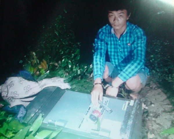 Hoàng Trọng Cảnh bên cạnh chiếc két sắt đã bị các đối tượng phá méo mó nhưng chưa lấy được tiền.