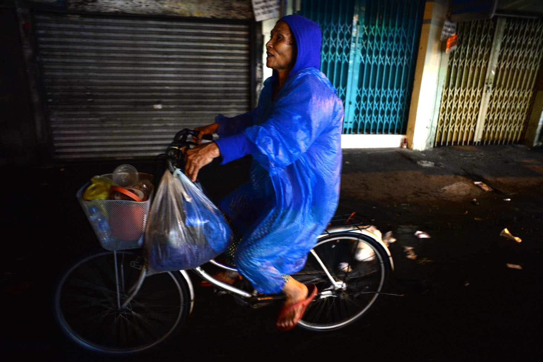 Những phận người nghèo trong đêm mưa Sài Gòn - 9 Bà Tư bán vé số ở khu quận 6, vừa nghe tin có phát cơm từ thiện bà mang vội chiếc áo mưa mỏng đạp xe đi xin về cho 2 mẹ con.