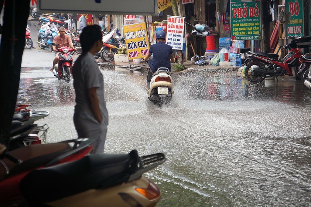 
Một nhân viên ở cửa hàng thuốc đứng ngán ngẩm nhìn cảnh người và xe bì bõm qua lại.
