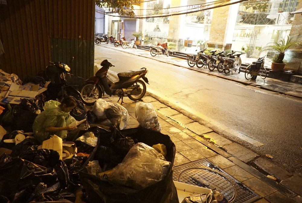 Chị Bùi Thị Chung người gốc Hà Đông đang đội mưa phân loại rác trên phố Hàng Bè sau một tối đi thu gom vất vả. Chung mới 23 tuổi đang thuê trọ tại khu chợ hoa Quảng An sống cùng mẹ và 2 đứa con nhỏ.