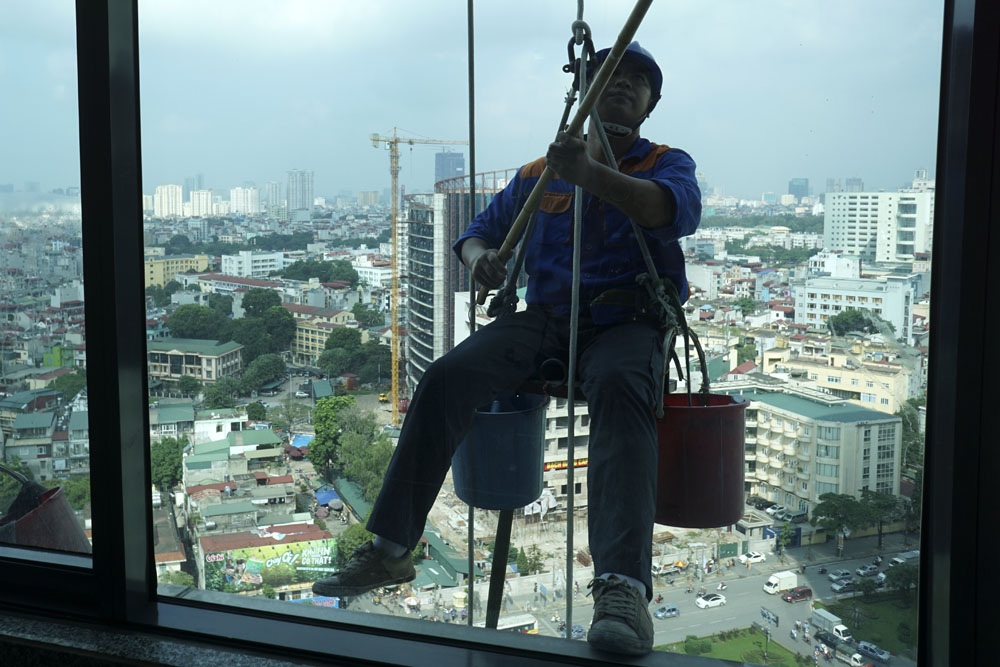 
Lỉnh kỉnh cùng người thợ là 2 xô đựng các loại dụng cụ như dụng cụ lau kính, hóa chất tẩy rửa, nước uống... Ở độ cao chóng mặt, mọi dụng cụ cần được bảo vệ chắc chắn để phòng tránh gây tai nạn cho người phía dưới và chính bản thân người thợ.
