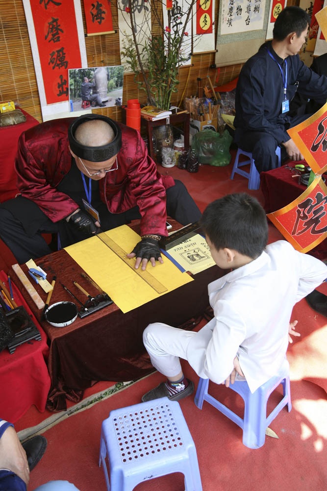 Xin chữ đầu năm, "ông đồ" vắng, "ông đồ "đông" - 7 Ông đồ Nguyễn Vũ Hồng Chi trong trang phục kết hợp kim cổ đang bắt đầu viết chữ hoan nghênh quý khách.