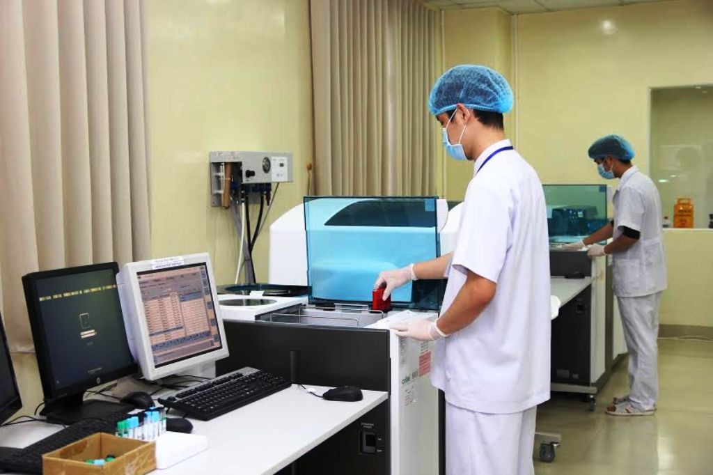 Thêm cơ hội cho người dân được khám chưa bệnh BHYT chất lượng cao - 2 Bác sỹ bệnh viện đang làm việc bên máy xét nghiệm tầm soát dị tật thai nhi sớm Immulite 2000....
