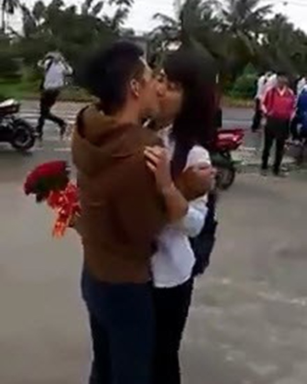 Hai bạn trẻ (bạn nữ mặc đồng phục học sinh) ôm hôn ngay trước cổng trường