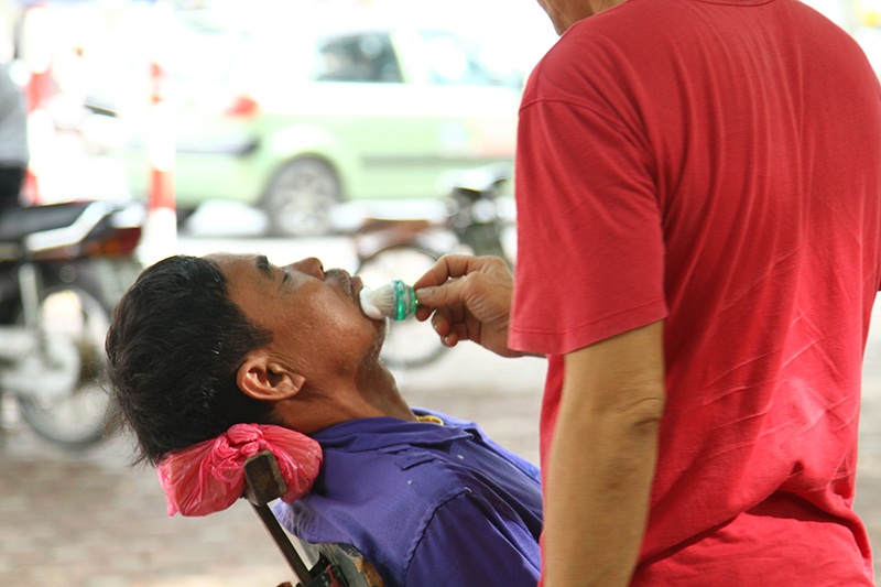 Một phụ huynh đến từ huyện Thanh Oai tranh thủ cắt tóc, cạo râu trong lúc chờ con đi thi.