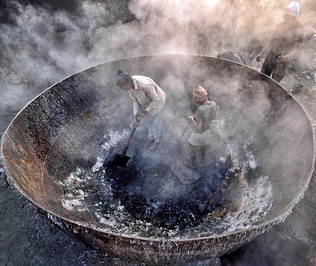 Hai công nhân đứng trong một nồi nung khổng lồ đang tỏa ra những làn khói dày đặc. Họ đang làm phân bón và thức ăn cho cá ở thành phố Kolkata, Ấn Độ. Ảnh chụp bởi Sudipta Dutta Chowdhury.