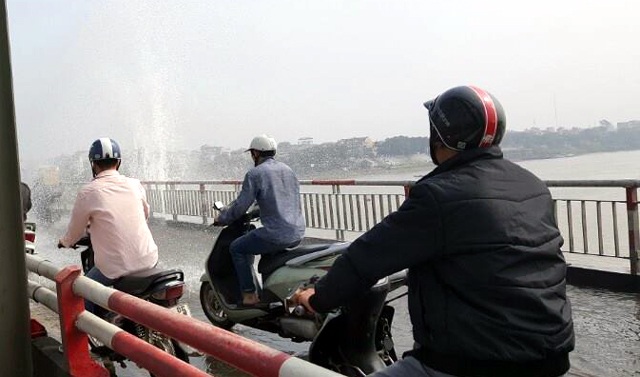 Nước phun xối xả trên cầu Chương Dương, người qua cầu mặc áo mưa giữa trời nắng - 1 Nước phun xối xả, lênh láng mặt cầu khiến người đi xe máy phải dừng lại.