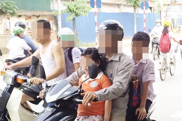 Hà Nội: Cha mẹ học sinh phải kí cam kết đội mũ bảo hiểm cho con - 1 Phụ huynh vô tư kẹp 3 trước cổng trường tại Hà Nội trong khi con em không đội mũ bảo hiểm. (Ảnh: Hạnh Nguyên)