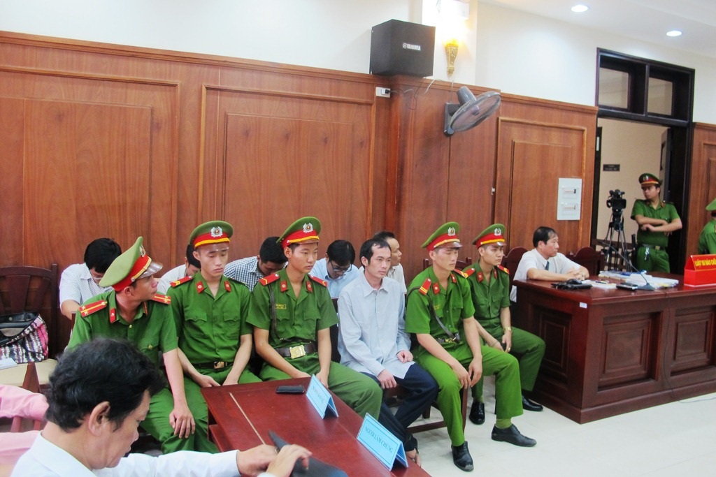 Các bị cáo (ngồi xen kẽ và sau lưng lực lượng công an) tại phiên tòa 