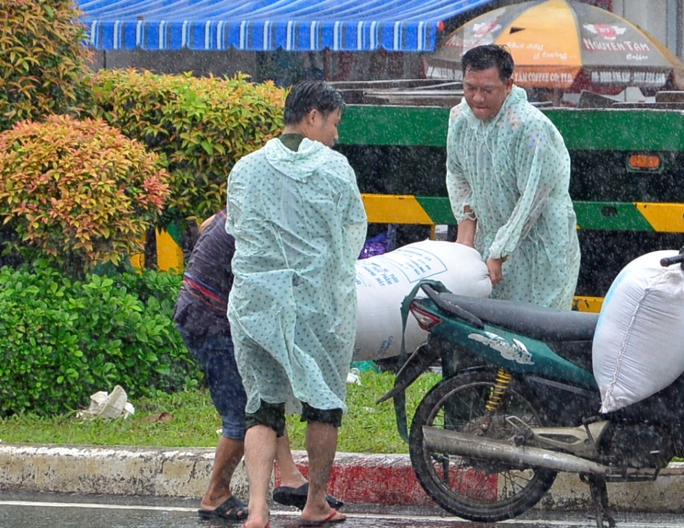 
Hai cán bộ công an phường mặc áo mưa ra đẩy xe, bê hàng hóa giúp dân.

