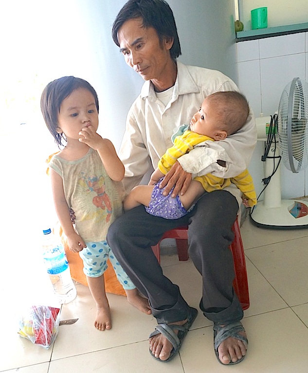 Xót xa chồng bế con nhỏ ngồi ở cửa bệnh viện xin tiền chữa bệnh cho vợ - 1 Hình ảnh người cha khốn khổ đến bước đường cùng phải bế con hai ngồi trước cổng ra vào để xin tiền nhập viện cho vợ.