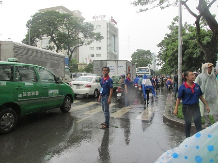 Sinh viên tình nguyện trường ĐH KHXHNV TPHCM đội mưa làm hàng rào hướng dẫn giao thông.