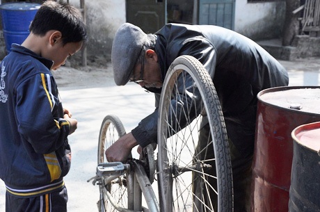 Ông Tâm cặm cụi sửa xe giúp cháu Tuấn, cháu là khách hàng thường xuyên của ông