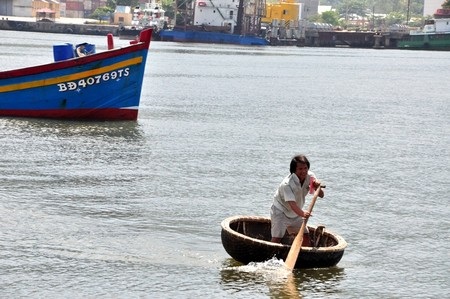 Một ngư dân tàu cá Bình Định vừa chèo thúng vừa cầm giấy trên tay, rất dễ rơi xuống nước