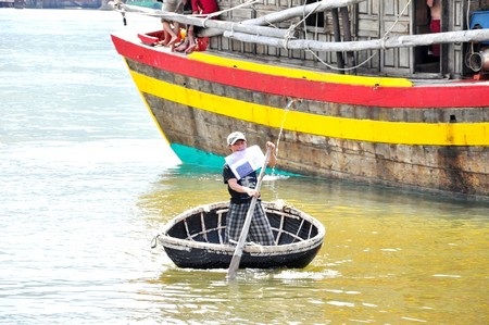 Một ngư dân vừa chèo thúng vừa ngậm giấy tờ vào miệng bơi vào bờ