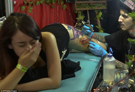 Cô gái nhăn nhó khi xăm hình. (Nguồn: Dailymail)