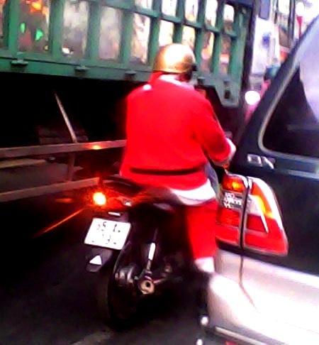 Một ông già Noel len lỏi giữa dòng xe cộ trên phố để chạy sô chuyển quà cho kịp thời gian.