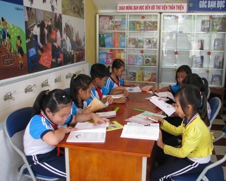 Đam mê đọc sách, em thêm phấn khởi đến trường - 2 Học sinh đang đọc sách tại góc thư viện nằm cạnh cầu thang của trường.