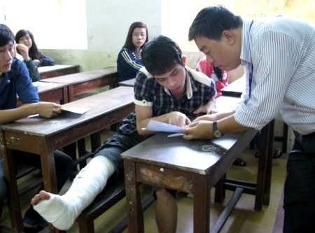 Lò cò một chân vẫn đến trường thi - 2 Giám thị xuống kiểm tra tên và giấy tờ của Khôi ngay tại chỗ ngồi theo đúng quy định.