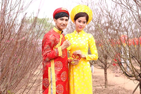 Một đôi bạn trẻ mặc trang phục áo dài, áo the chụp ảnh giữa vườn đào