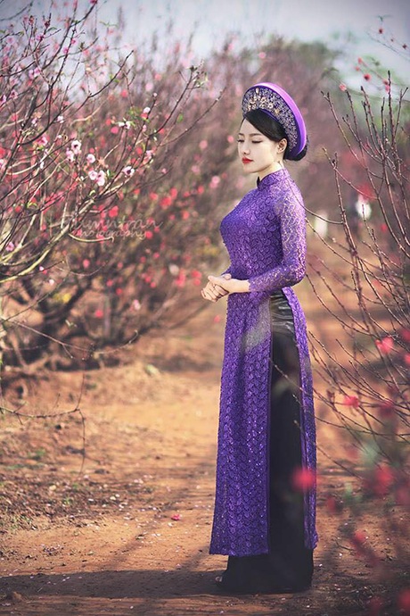 Cô khoác lên mình chiếc áo dài tím nổi bật giữa vườn đào hồng thắm