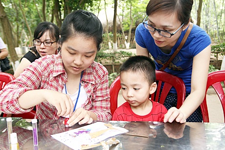 Một bạn sinh viên trường ĐH Hà Nội hướng dẫn em nhỏ trang trí chuồn chuồn gỗ