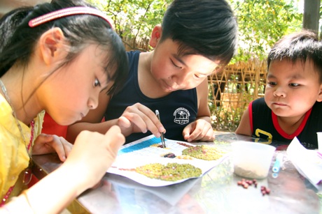 Các em nhỏ say sưa “tô màu” tranh bằng ngũ cốc thể hiện các di sản văn hóa của Đông Nam Á.