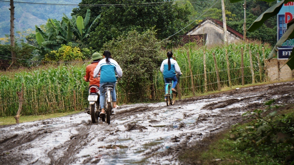 Các em học sinh đi xe đạp giữa bùn lầy lội.