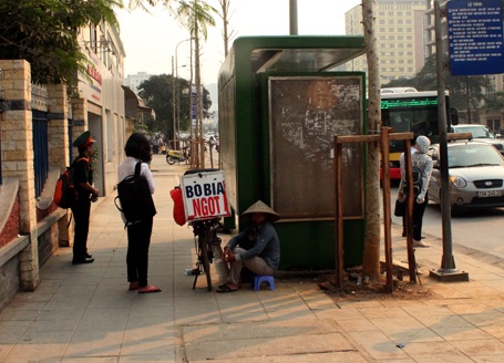 Một người bán hàng trốn nắng sau nhà chờ xe buýt. (Ảnh: Quang Phong)