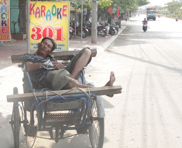 Bác tài xích lô tranh thủ giấc ngủ trưa dưới bóng mát nhỏ bé trên đường Nguyễn Thái Học