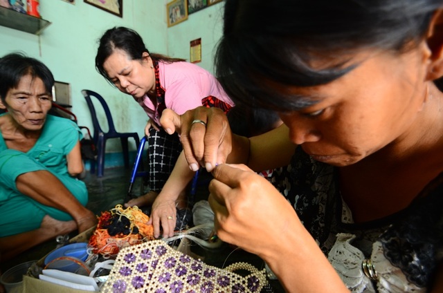 Tấm lòng vàng của nữ vận động viên khuyết tật - 2 Chị Phạm Thị Bích Loan bị tật ở mắt nên việc xỏ chỉ qua lỗ trên hạt cườm khá khó khăn. Cô Tư bị cụt tay nên cũng chỉ biết ngồi phân loại, sắp xếp chứ không trực tiếp gia công được. Lúc này cô Tư vừa đi bán vé số về nên ngồi vào phụ mọi người.