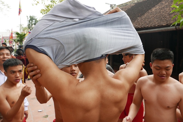 Sức mạnh "đội quân đánh giặc ngoại xâm" ở hội pháo Đồng Kỵ - 3
Trong khi đoàn rước pháo đang đi dọc làng trong bầu không khí lễ hội vô cùng sôi động, tại một khoảng sân yên tĩnh bên trong khuân viên đình, các thanh niên lặng lẽ chuẩn bị cho nghi lễ rước quan đám. Đây là những chàng trai tuổi 18 trở lên, thuộc nhiều dòng họ khác nhau trong làng Đồng Kỵ, sẽ đóng vai trò là các trai đinh kiệu đỡ 4 ông đám diễn múa ở phần cao trào của lễ hội.