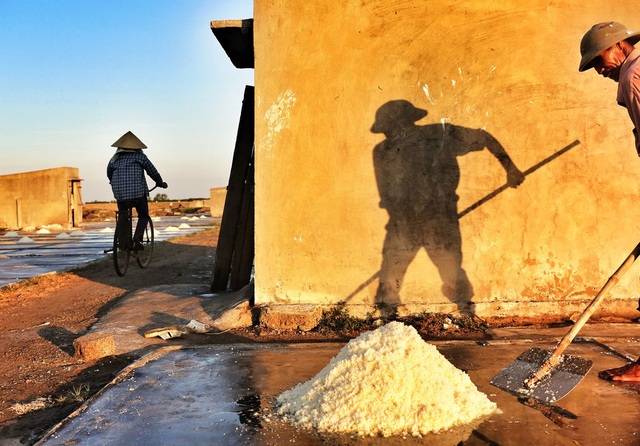 Những hình ảnh xuất sắc của nhiếp ảnh gia Việt đăng trên National Geographic - 7 Ở Việt Nam vùng ven biển miền Trung và miền Nam nghề làm muối dùng phương pháp phơi nước. Người dân thường đào ao hoặc hồ cạn rồi thông cho nước biển chảy vào đầy, sau đó đóng lại. Khi ruộng muối bốc hơi, nước sẽ cạn và còn lại hạt muối. Diêm dân (người làm muối) sẽ cào muối thu hoạch và đem bán. Ảnh chụp một người diêm dân ở biển Diễn Châu, Nghệ An. (Click vào đây để xem ảnh kích thước lớn)