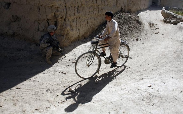 Đường đến trường gian nan của học sinh các nước - 14 Một học sinh ở tỉnh Logar, Afghanistan đạp xe đi học trong khi một binh sĩ thuộc quân đội Mỹ cầm súng chiến đấu với phiến quân.