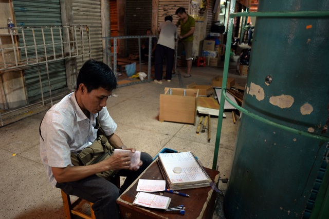 Anh Minh (48 tuổi), chủ cửa hàng quần áo trong chợ Bình Tây đang tính toán lại sổ sách để dời ra chợ tạm.