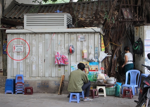 Nguy hiểm rình rập từ những bốt điện trên phố Hà Nội - 1 Mặc dù có biển cảnh báo nguy hiểm, không được lại gần ( ở vòng tròn đỏ) tại bốt điện này, nhưng người bán hàng nước và vị khách này vẫn ngồi sát (Ảnh chụp tại vỉa hè phố Vũ Tông Phan).