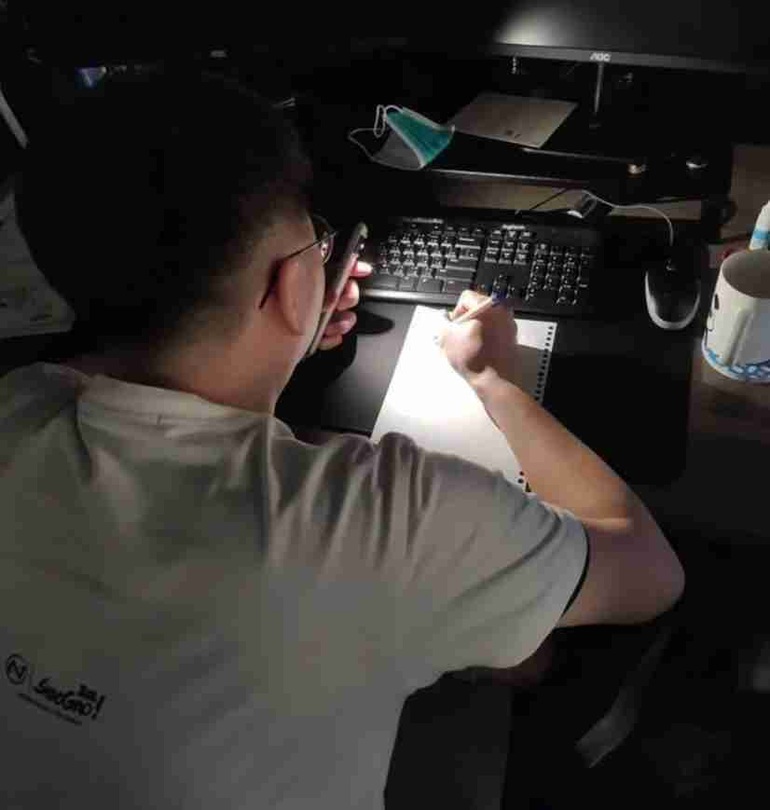 Một lập trình viên bật đèn pin smartphone và viết mã lập trình trên giấy (Ảnh: Qdmana).