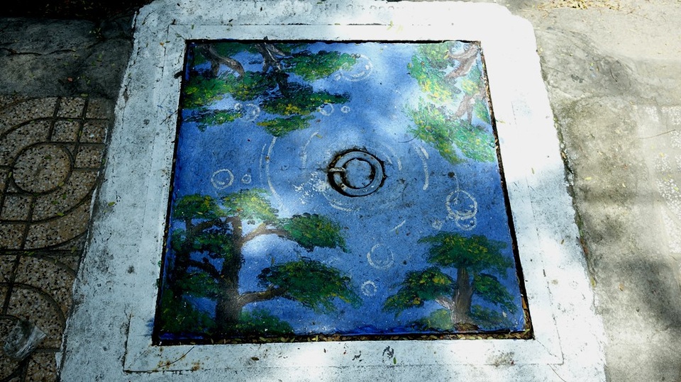 Ngắm hàng cây in bóng nước qua… nắp cống.