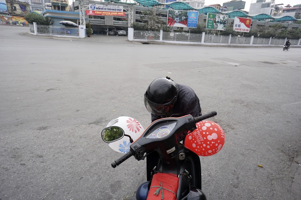 Người lái xe ôm rảnh việc buộc 2 quả bóng nhiều màu trang trí cho chiếc xe của mình.