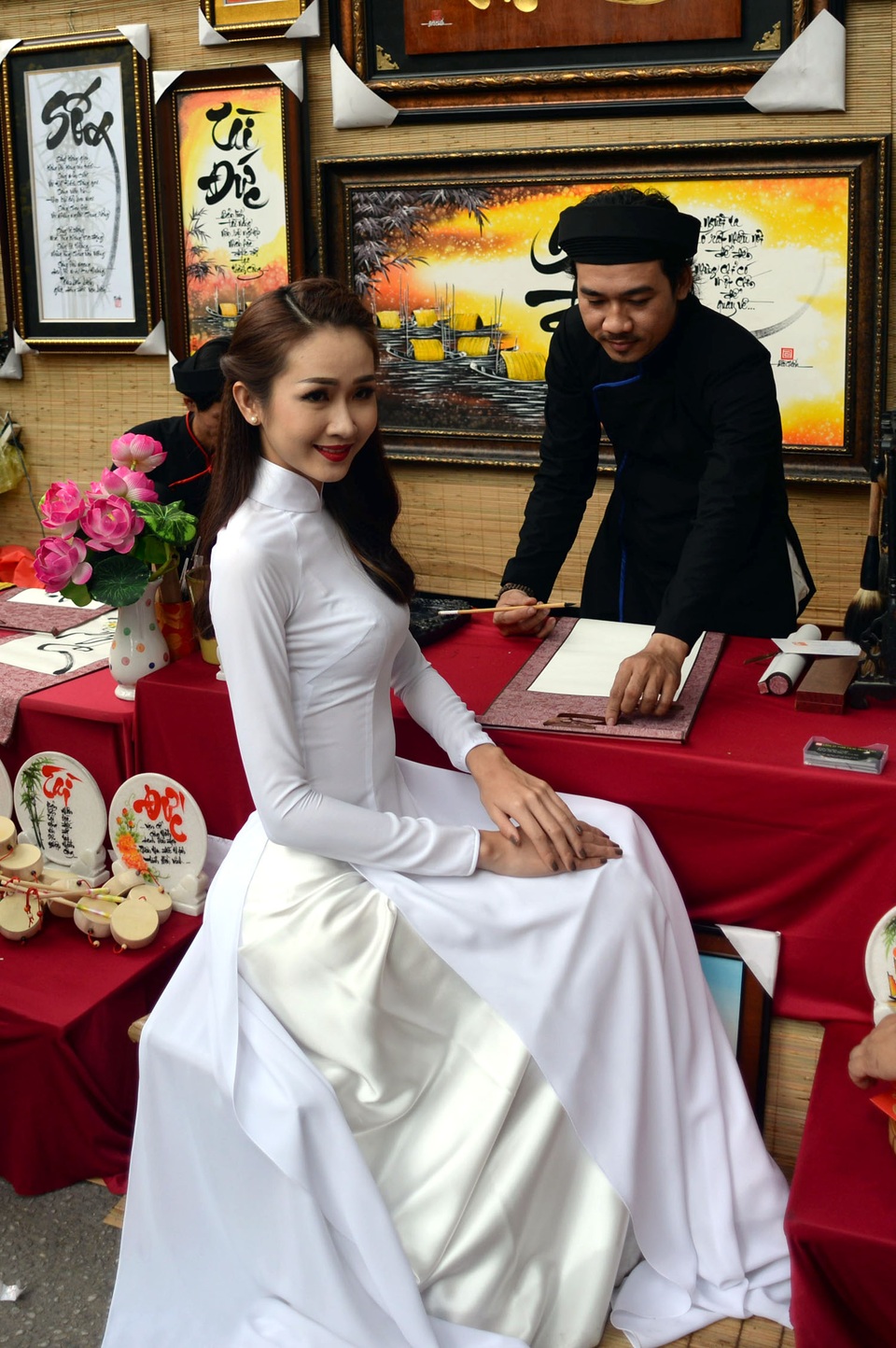 Thiếu nữ xinh đẹp áo dài trắng chụp hình trước bàn viết thư pháp của thầy đồ.