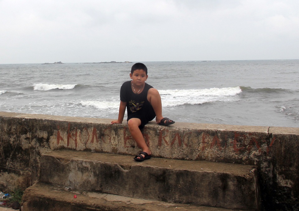 Một bé trai ở thôn Nam Hải thản nhiên ngồi chơi trên kè chắn sóng.